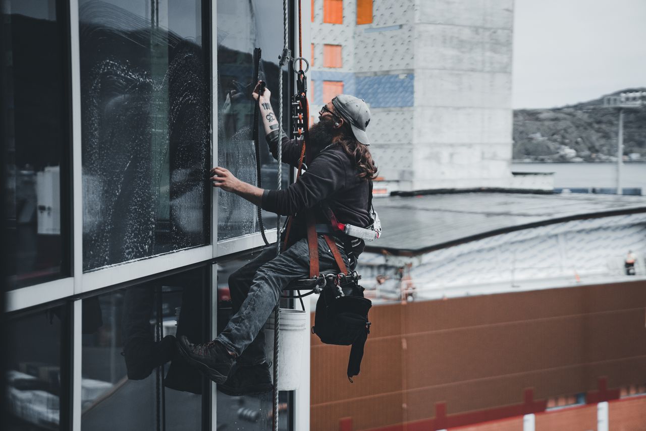 Un homme nettoie les vitres d'un gratte-ciel à l'aide d'un harnais, illustrant le travail en hauteur en milieu urbain.