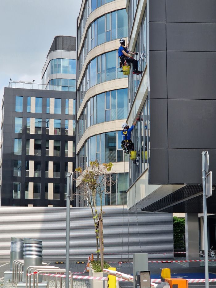 Deux travailleurs nettoient les fenêtres d’un immeuble de bureaux élevé dans un environnement urbain.